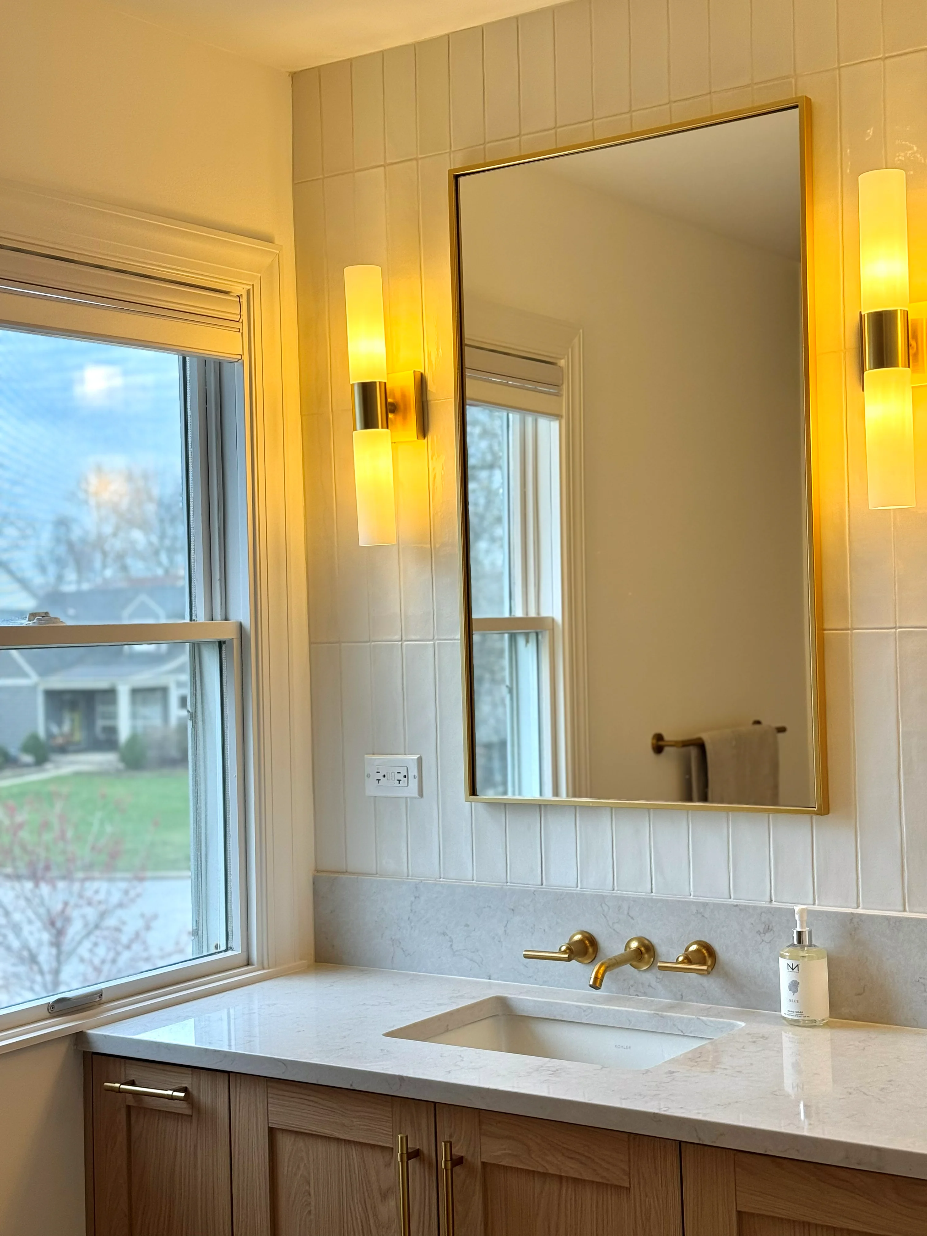 Bathroom with marble countertop, brass fixtures, shiplap walls, and framed mirror