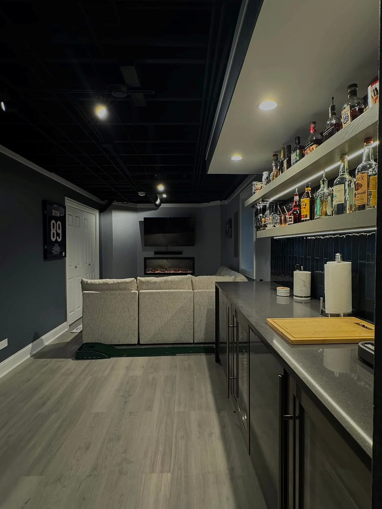Finished basement bar with dark cabinetry, floating shelves, vinyl plank flooring, and recessed lighting