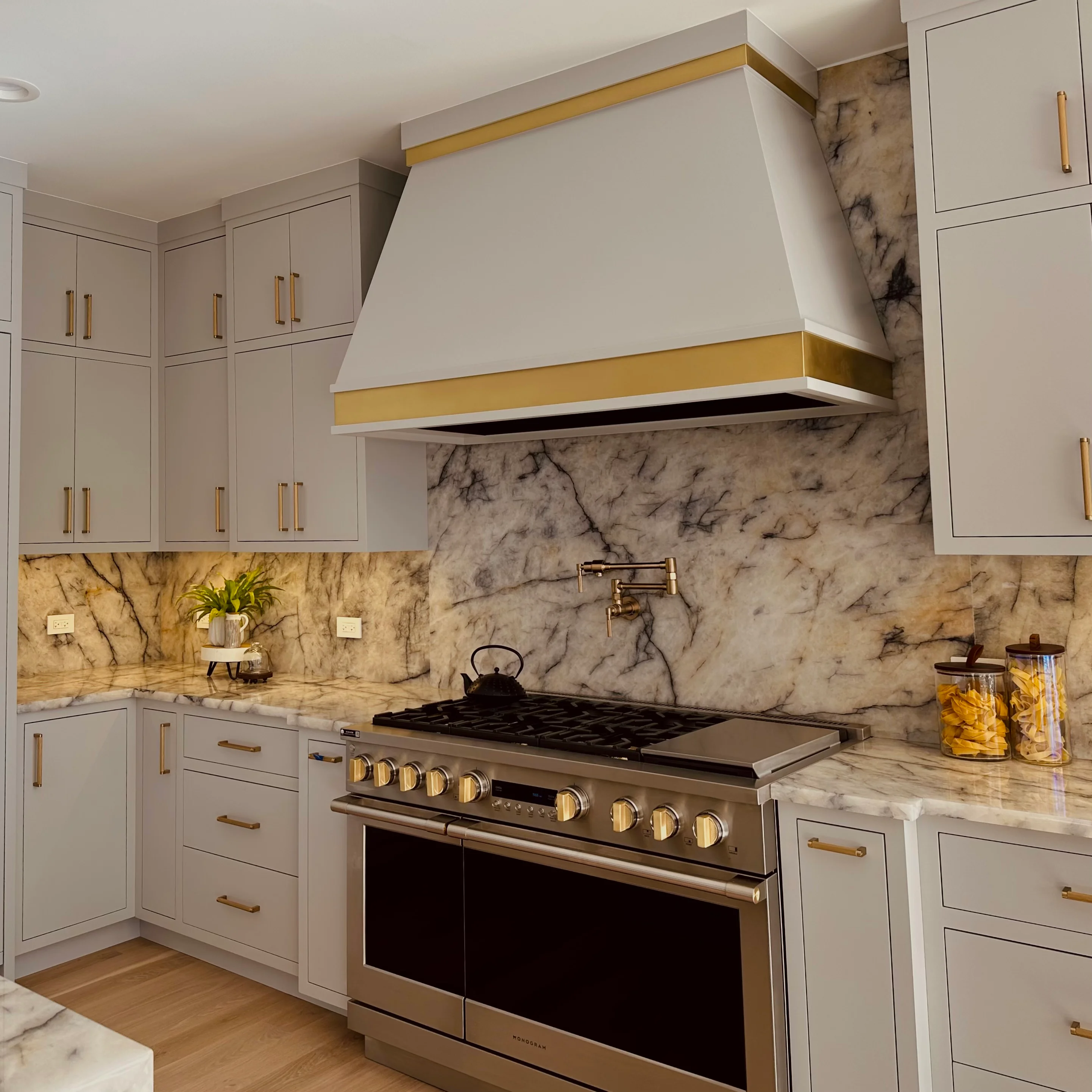 Modern kitchen with white cabinets, marble backsplash, and custom brass-trimmed hood