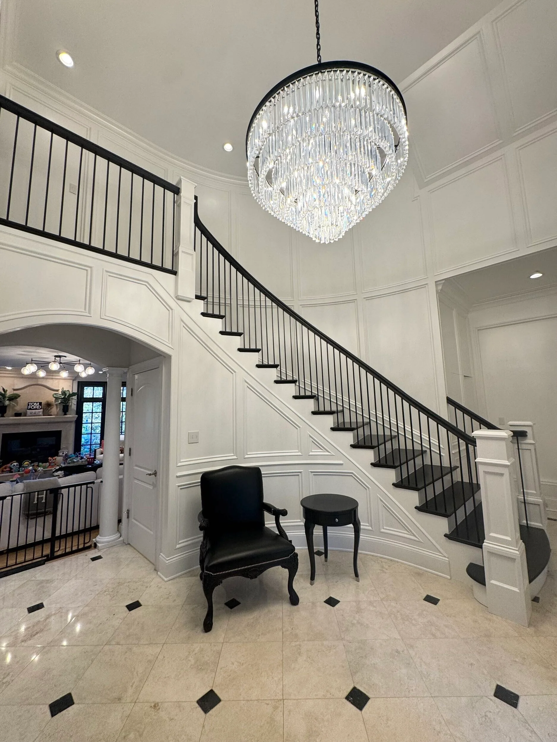 Luxury foyer with curved staircase, white paneling, and crystal chandelier