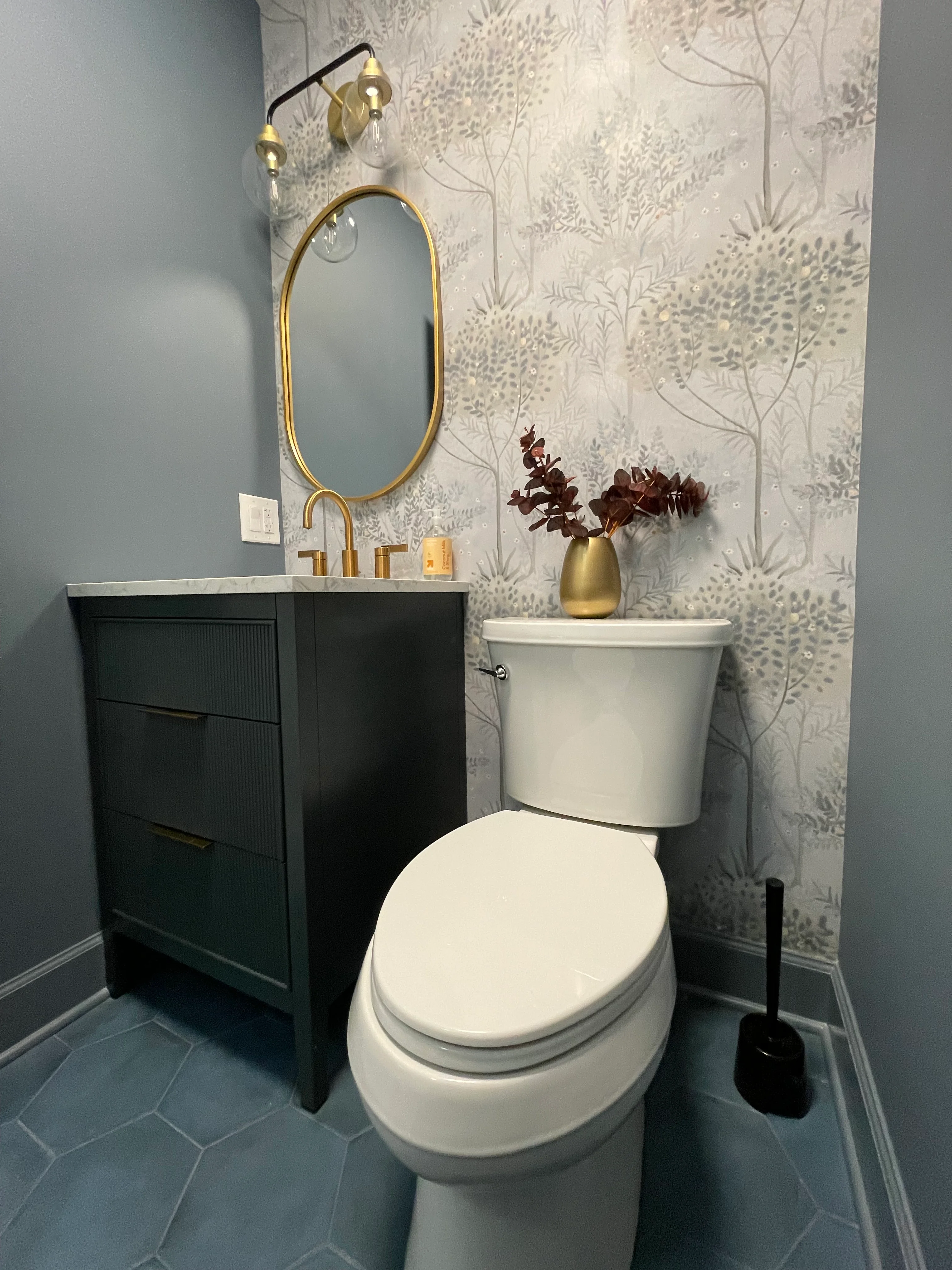 Black vanity with white quartz, brass mirror and sconce, botanical wallpaper, slate tile floor