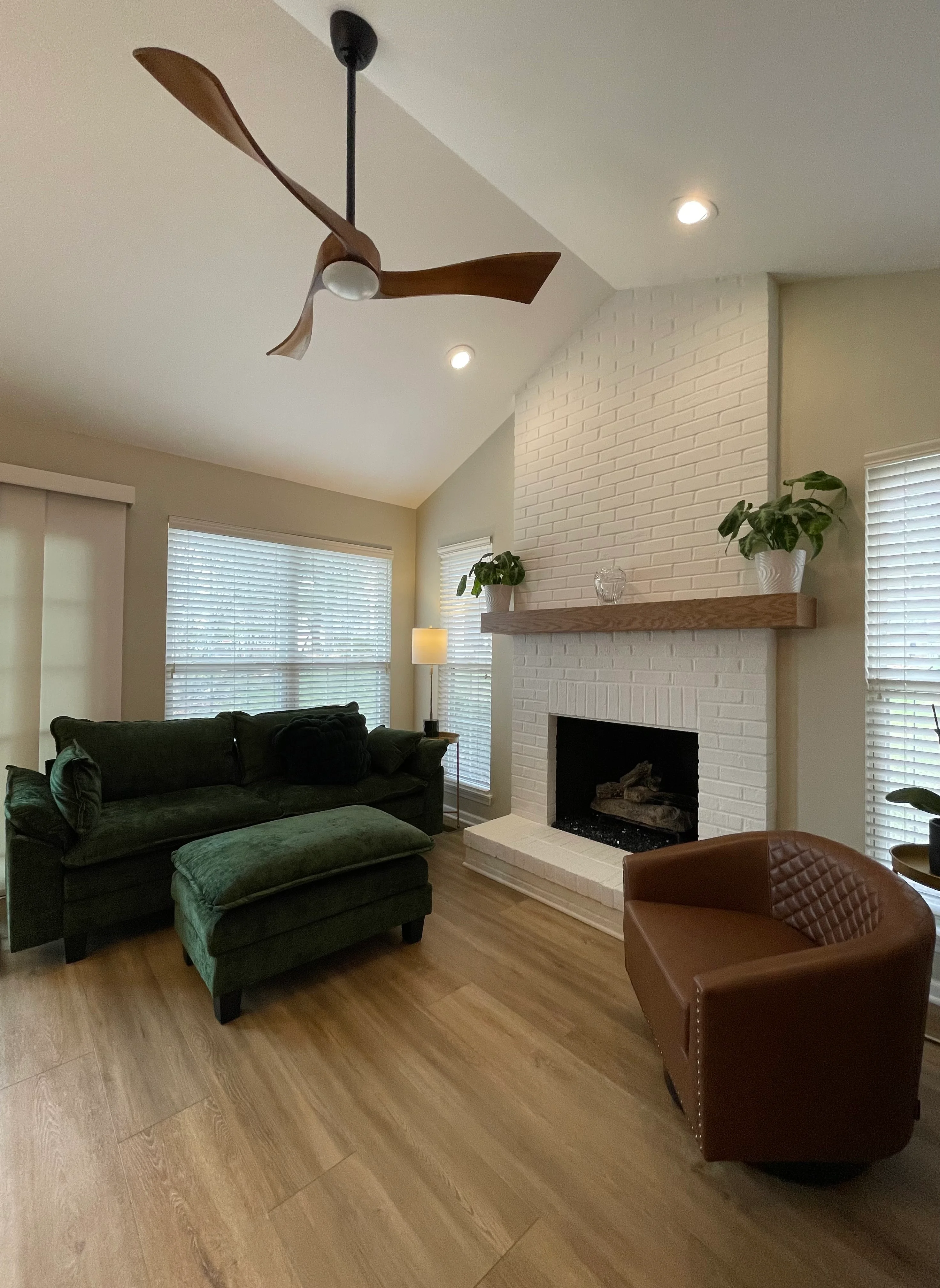 Modern living room with white brick fireplace, wood mantel, ceiling fan, recessed lighting, and hardwood flooring