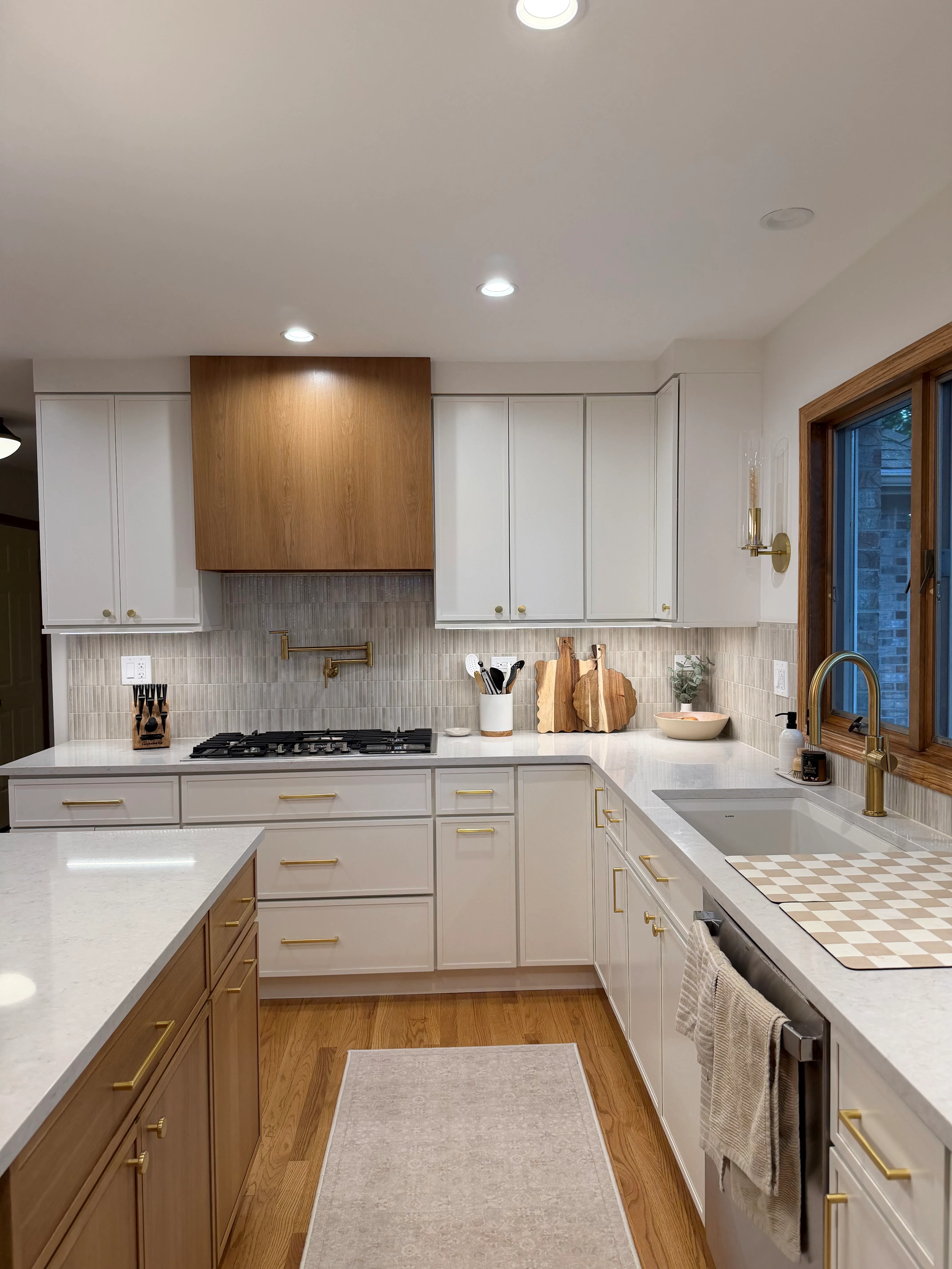 White kitchen cabinets with brass hardware, walnut range hood, subway tile backsplash, quartz counters, and hardwood flooring