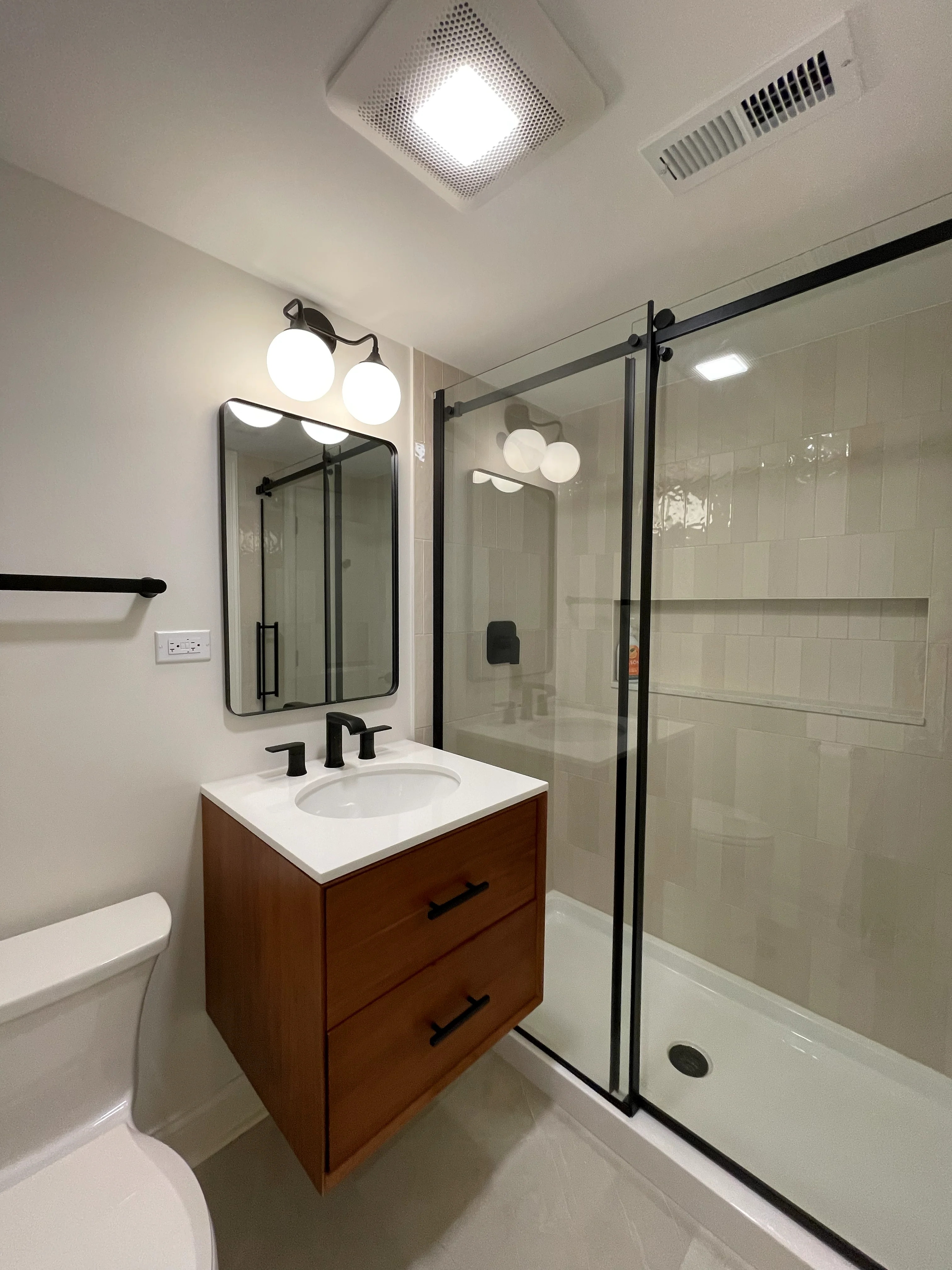 Modern bathroom with wood vanity, quartz countertop, frameless glass shower, and subway tile walls