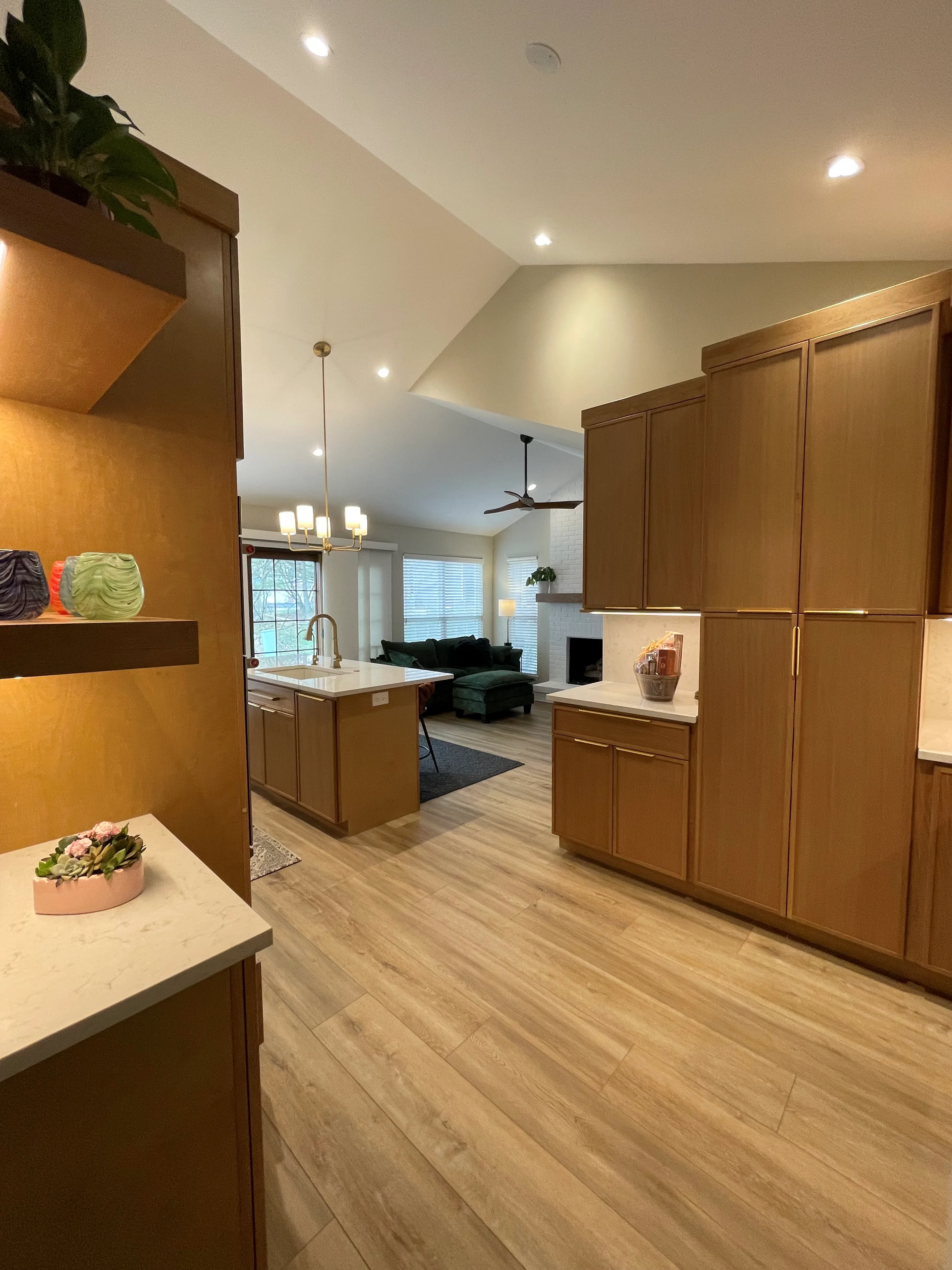 Modern kitchen with wood cabinetry, quartz counters, vinyl plank flooring, and open living area