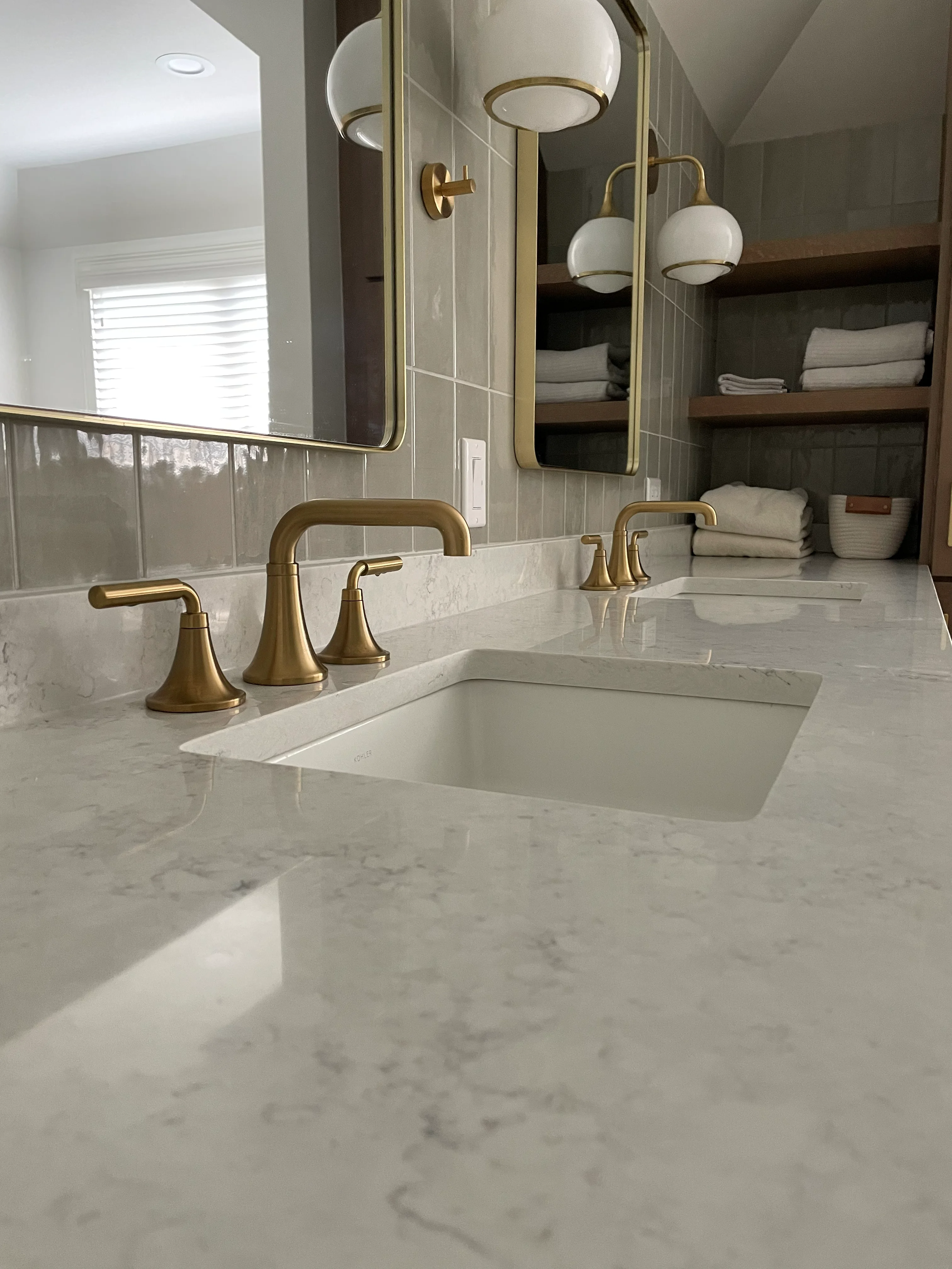 Marble countertop bathroom with dual sinks, brass fixtures, subway tile, and built-in shelving
