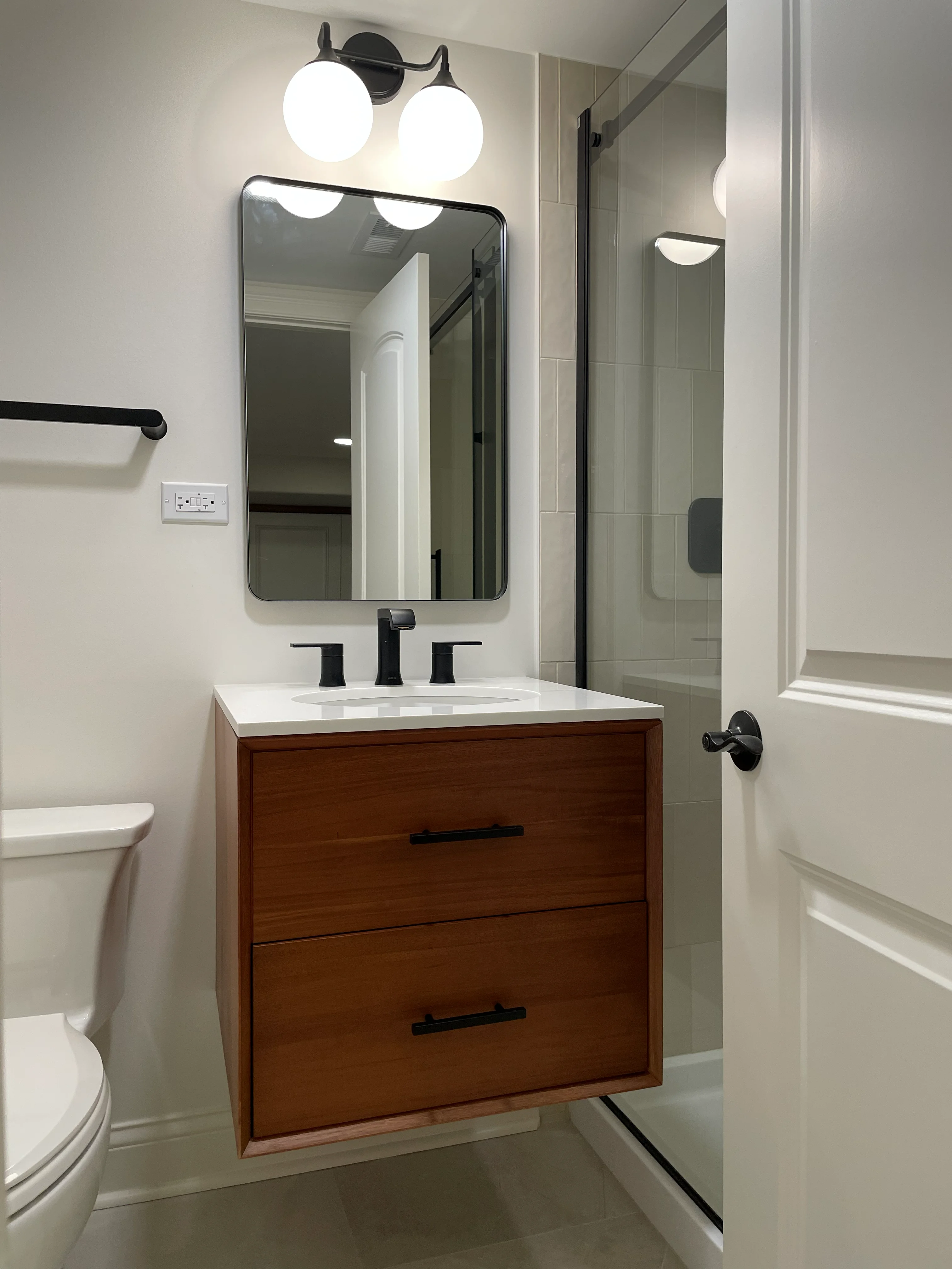 Modern bathroom with wood vanity, white quartz countertop, black fixtures, and tile shower