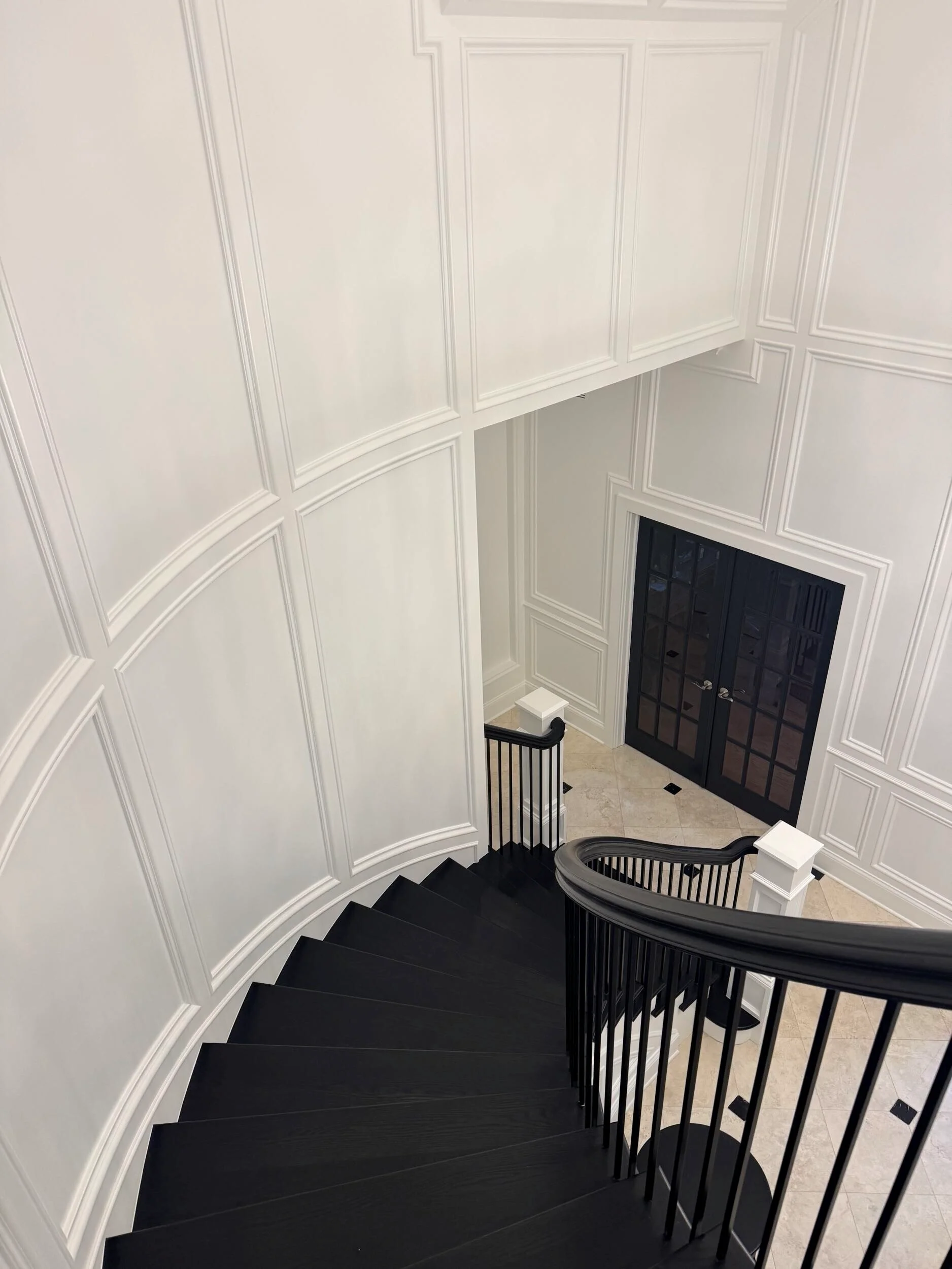 White wainscoting with molding, curved black staircase with spindles and handrail in stairwell