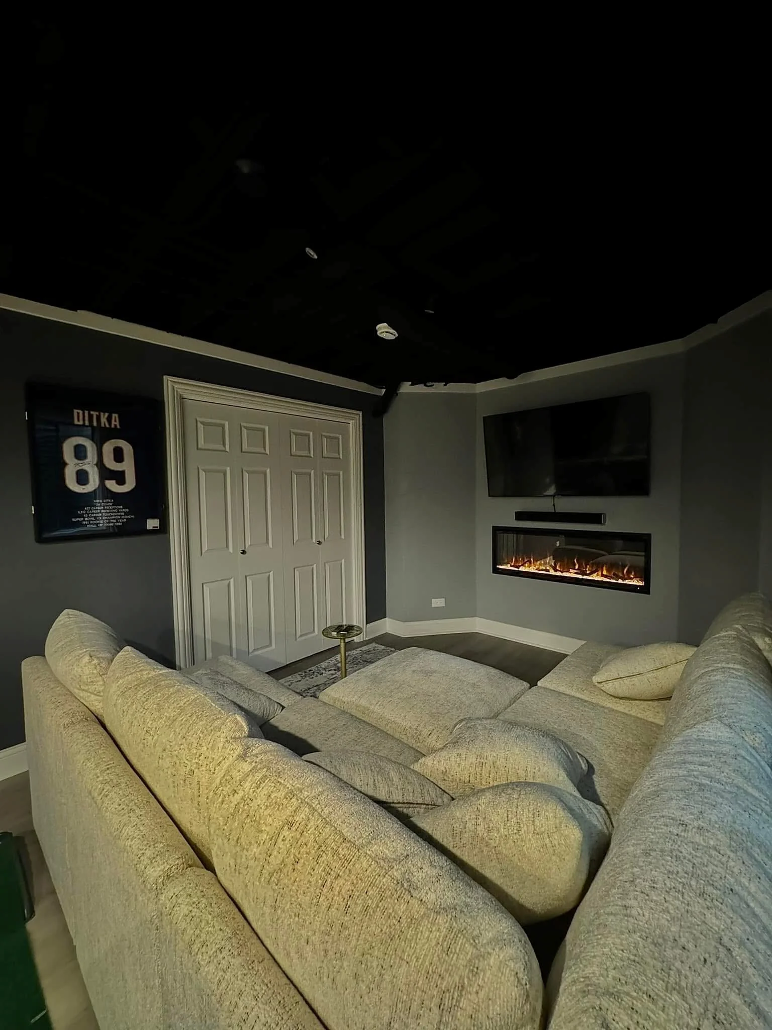 Finished basement media room with gray walls, electric fireplace, recessed lighting, and white closet doors