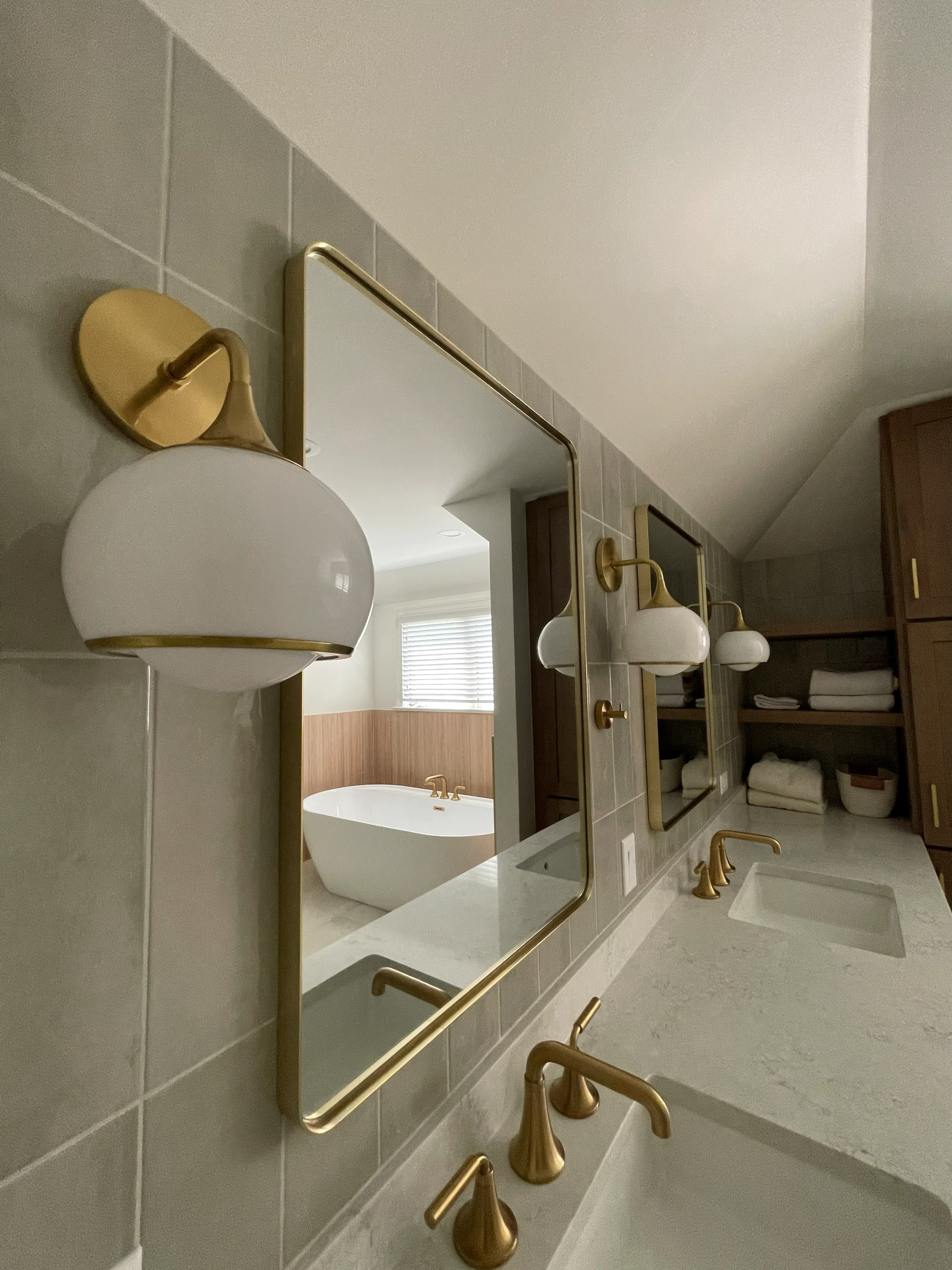 Modern bathroom with white subway tile, marble counters, brass fixtures, and dual vanities with mirrors