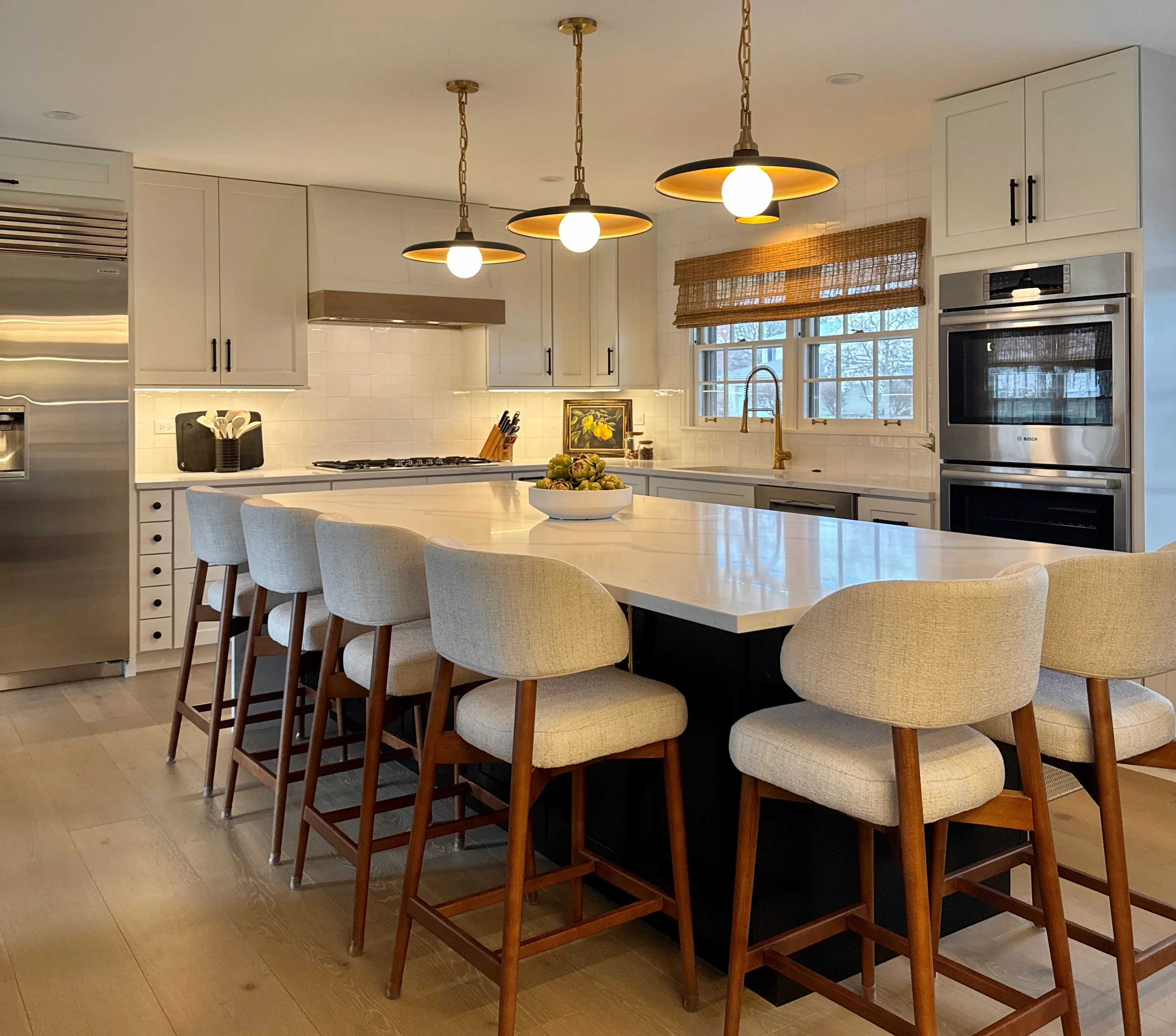 Modern kitchen with white cabinetry, quartz island, brass pendants, and wood-framed seating
