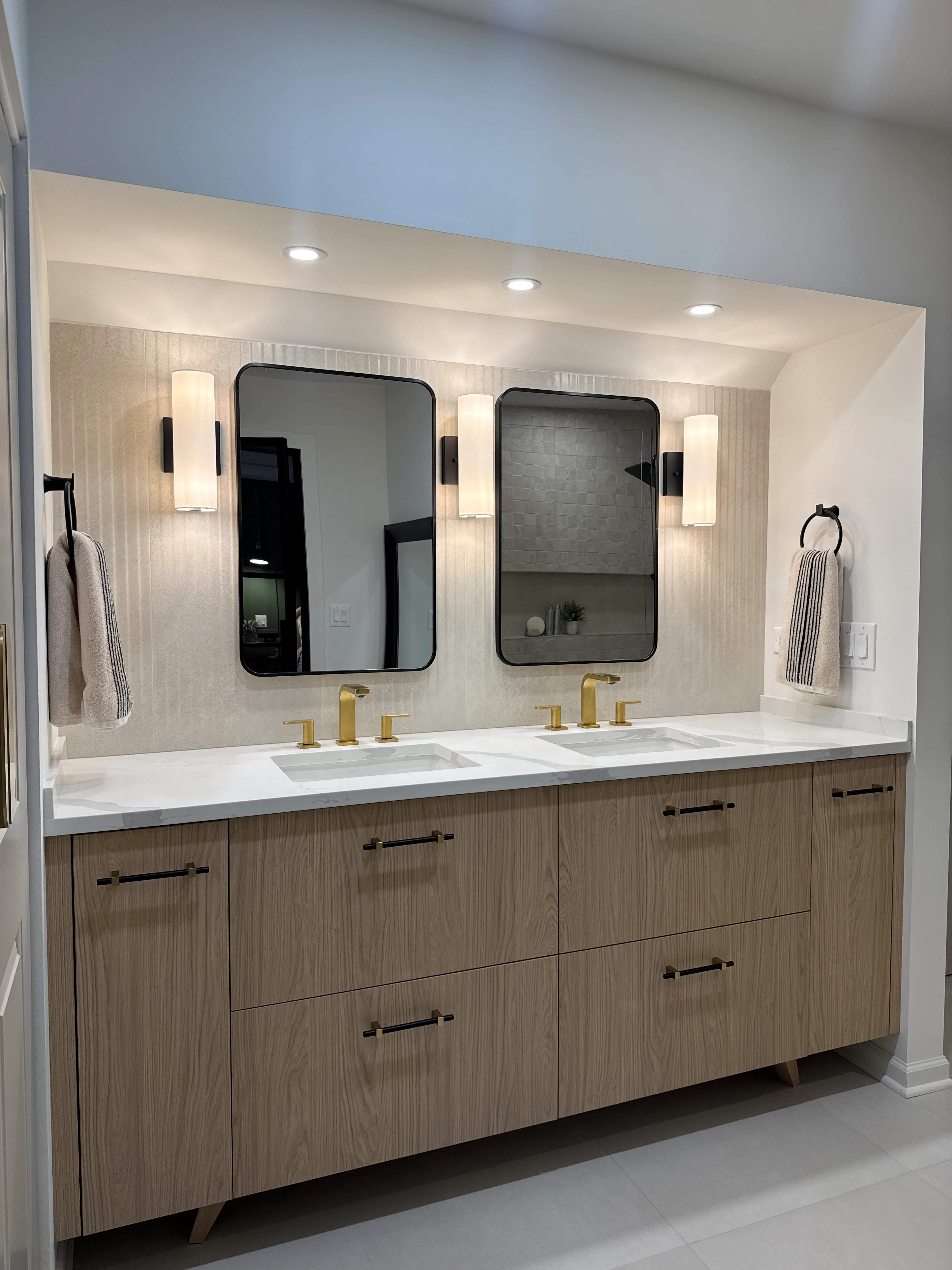 Double vanity with walnut cabinetry, white quartz countertop, brass fixtures, and black-framed mirrors