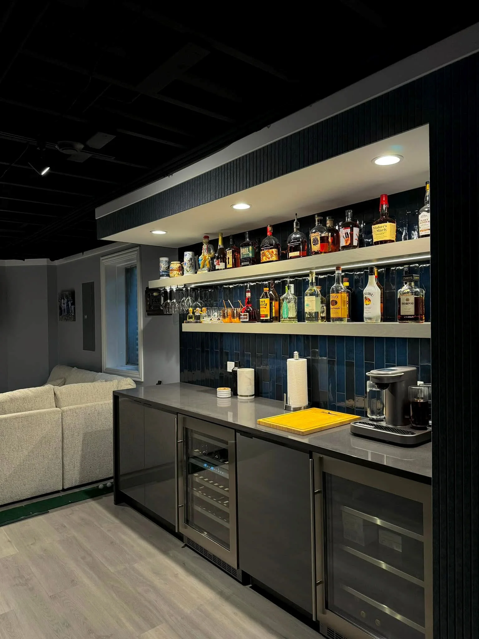 Modern home bar with floating shelves, LED lighting, dark shiplap wall, and glass-front wine coolers