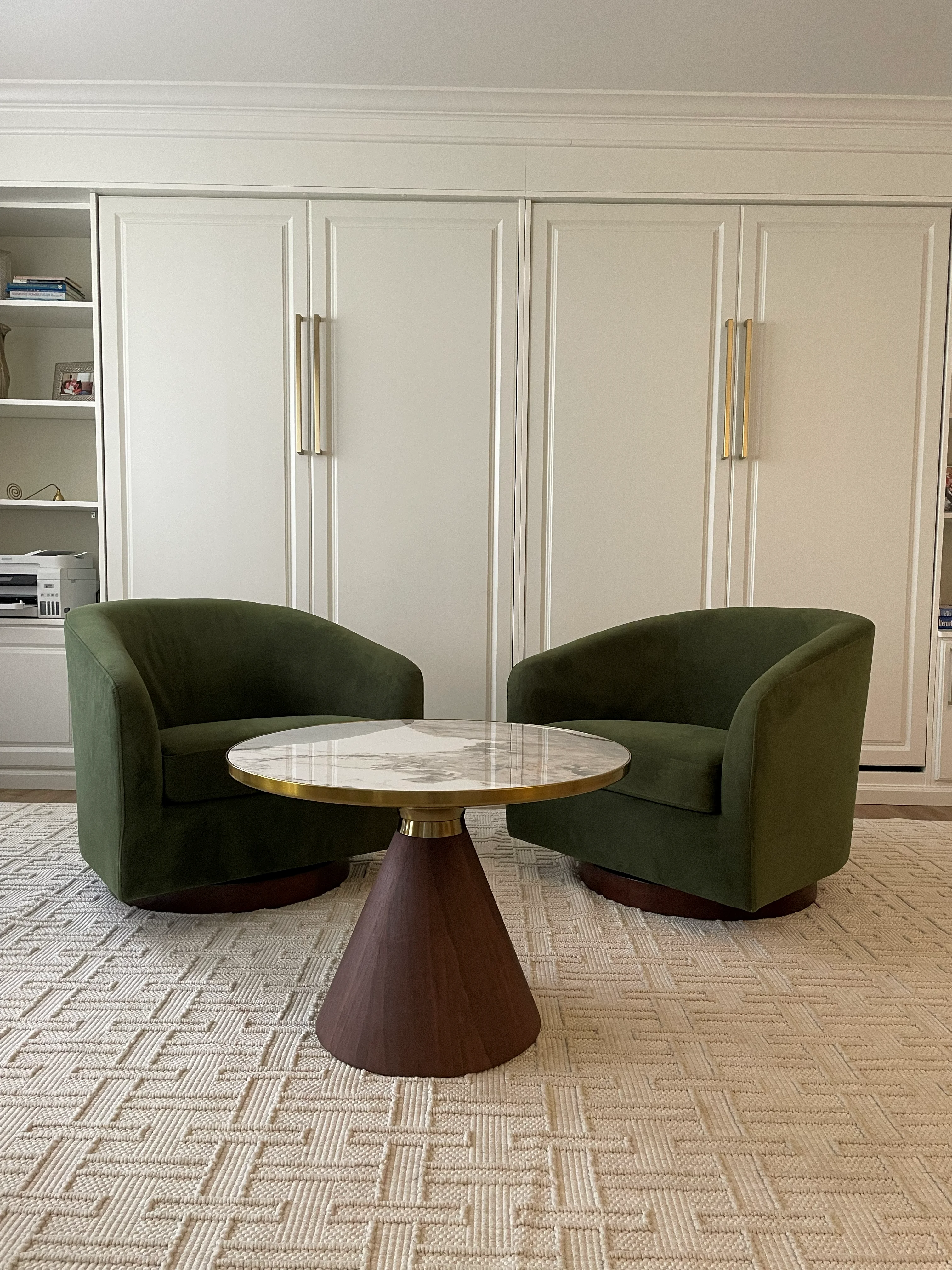 Modern office with white cabinetry, marble table, green chairs, and geometric carpet flooring
