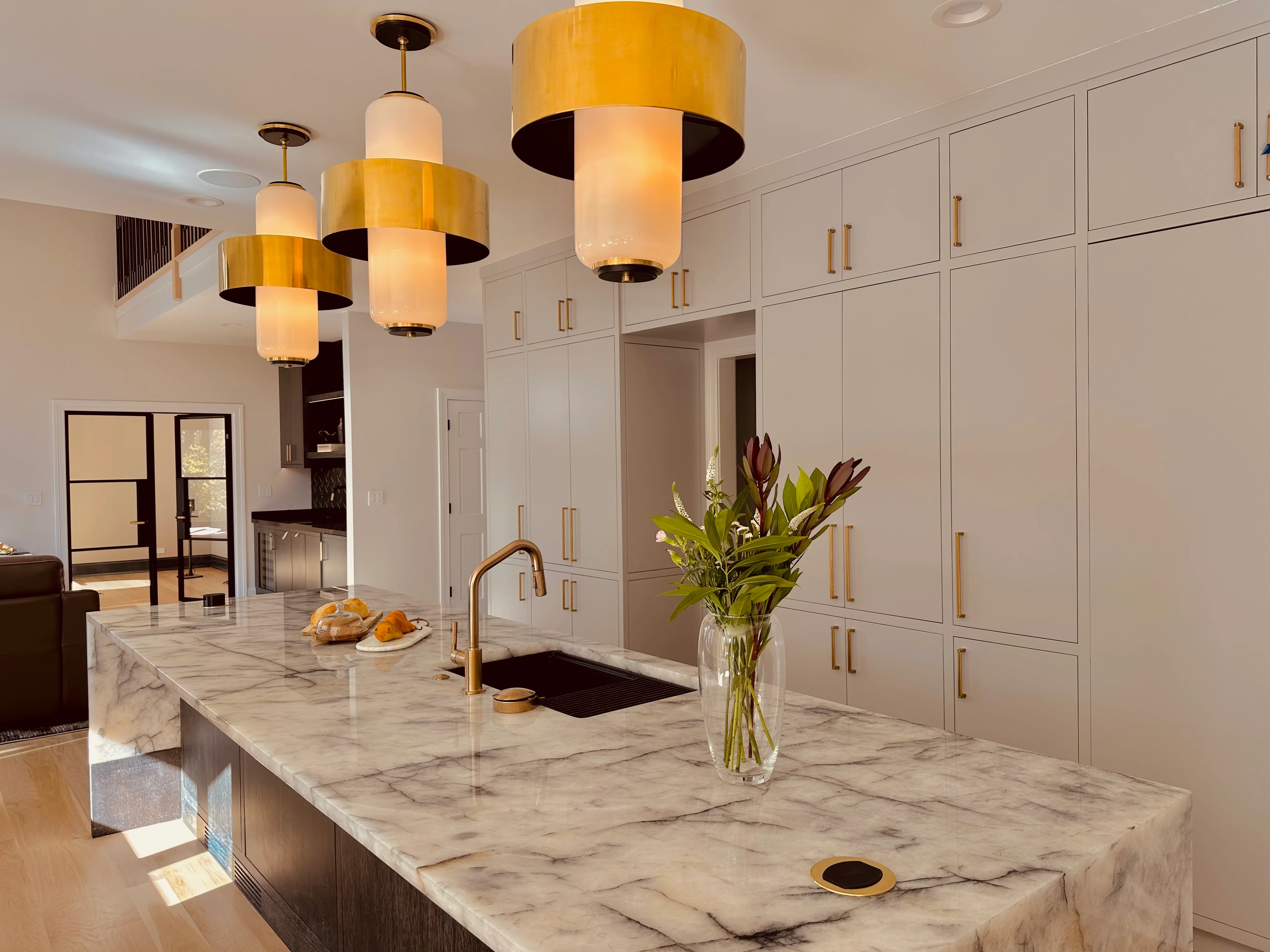 Modern kitchen with marble counters, white cabinetry, and brass pendant lights