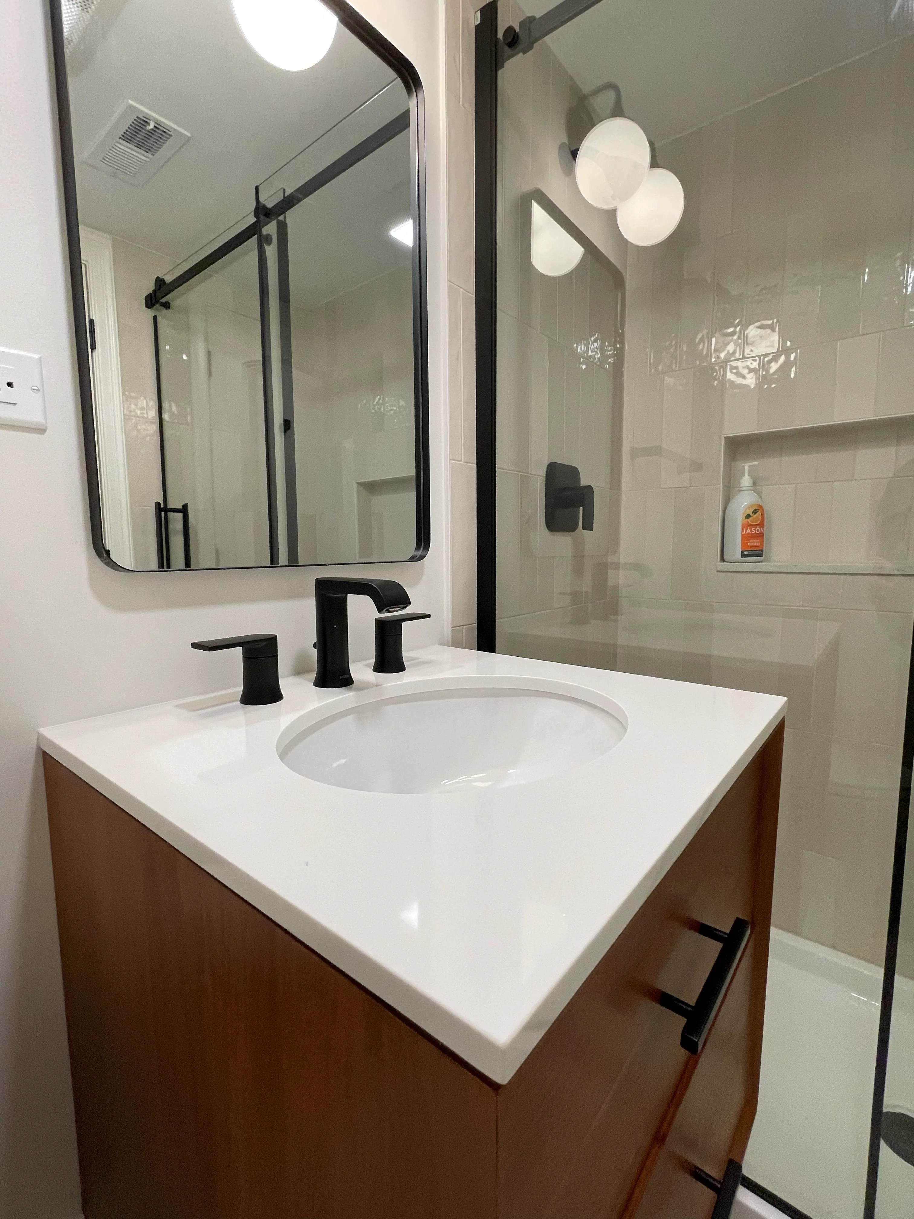 Modern bathroom with wood vanity, white quartz countertop, black fixtures, and glass shower enclosure