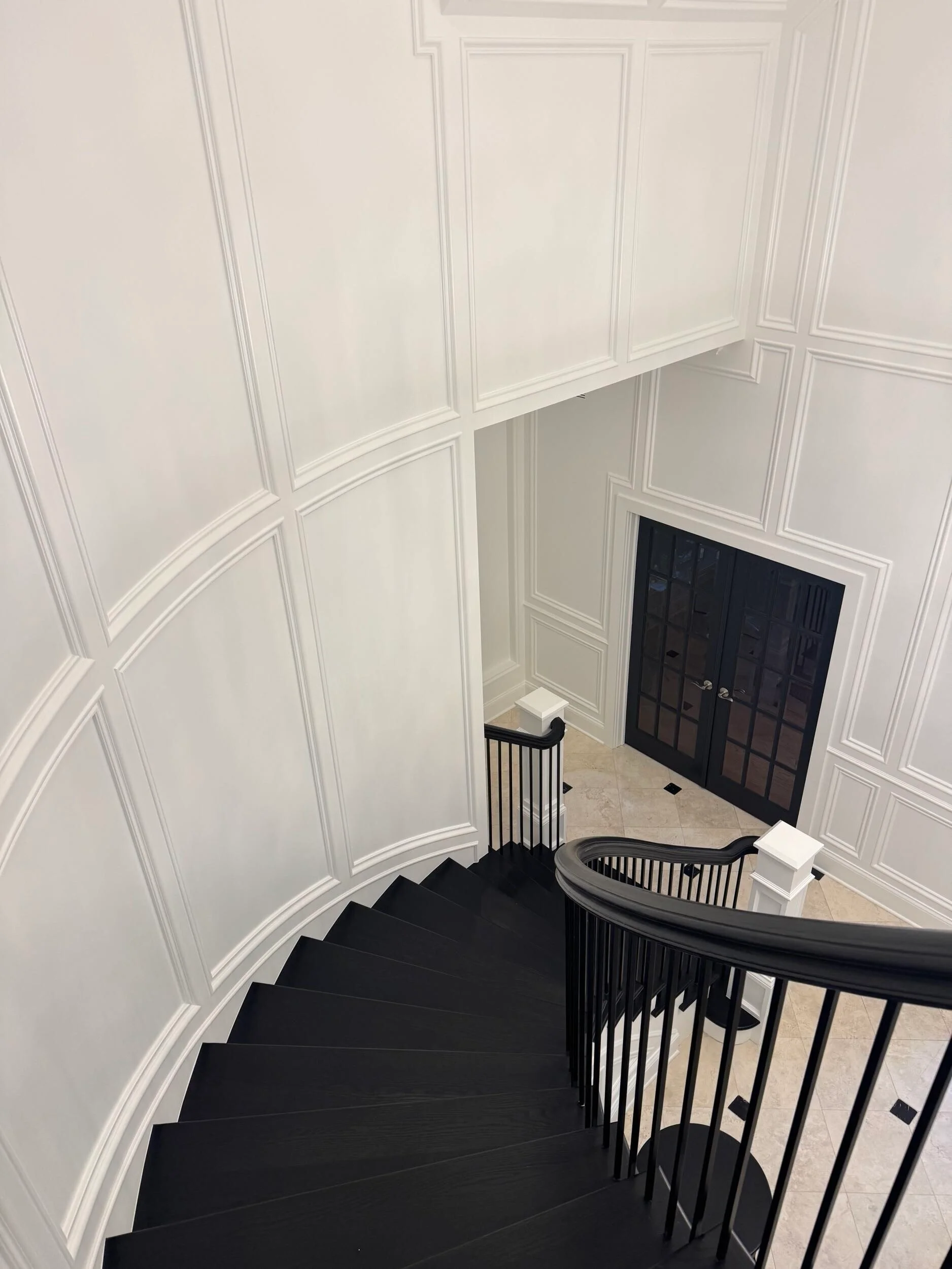 Curved black staircase with white wainscoting walls and black metal railings in modern foyer