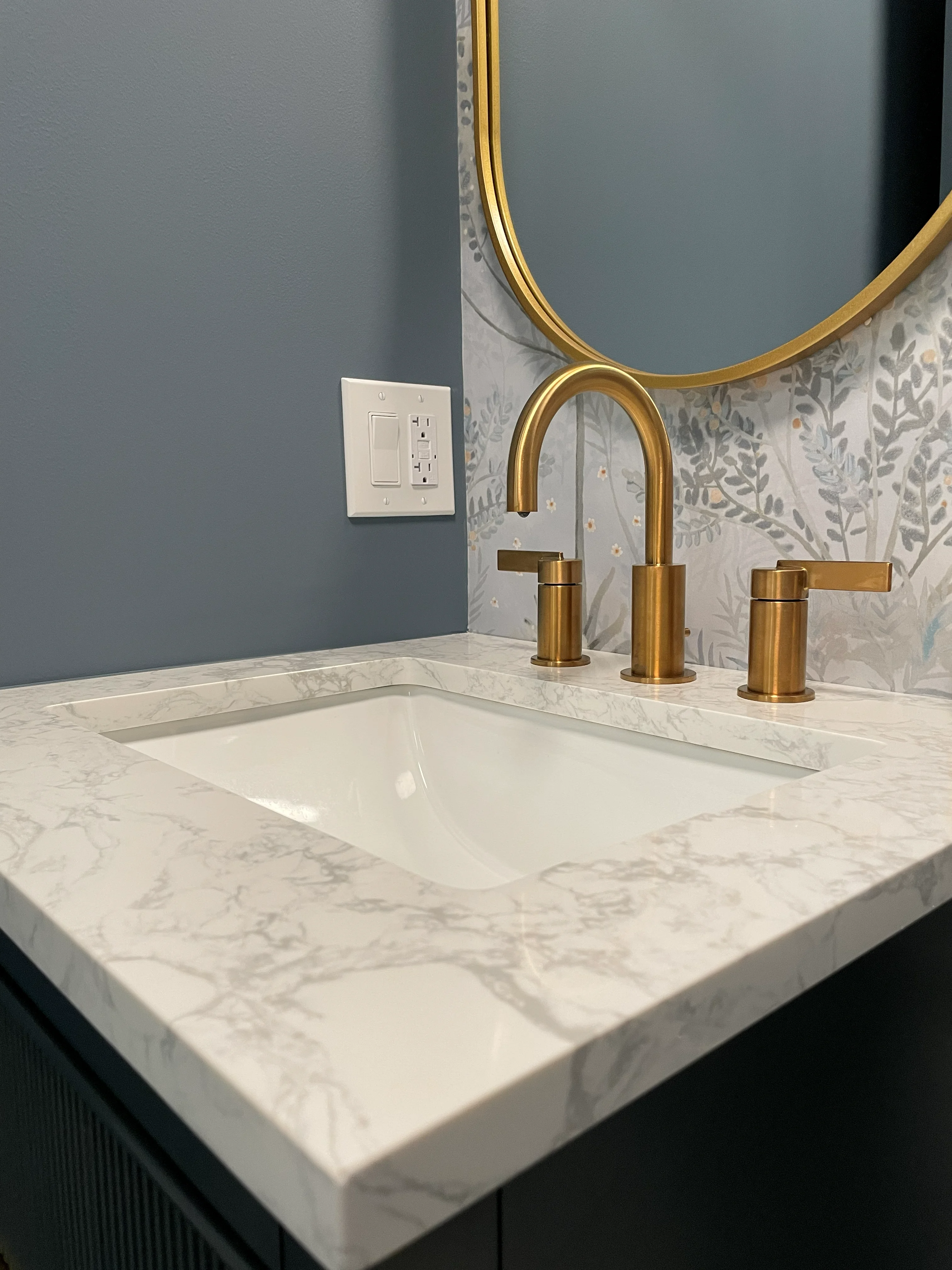 Marble vanity with brass faucet, undermount sink, and botanical tile backsplash