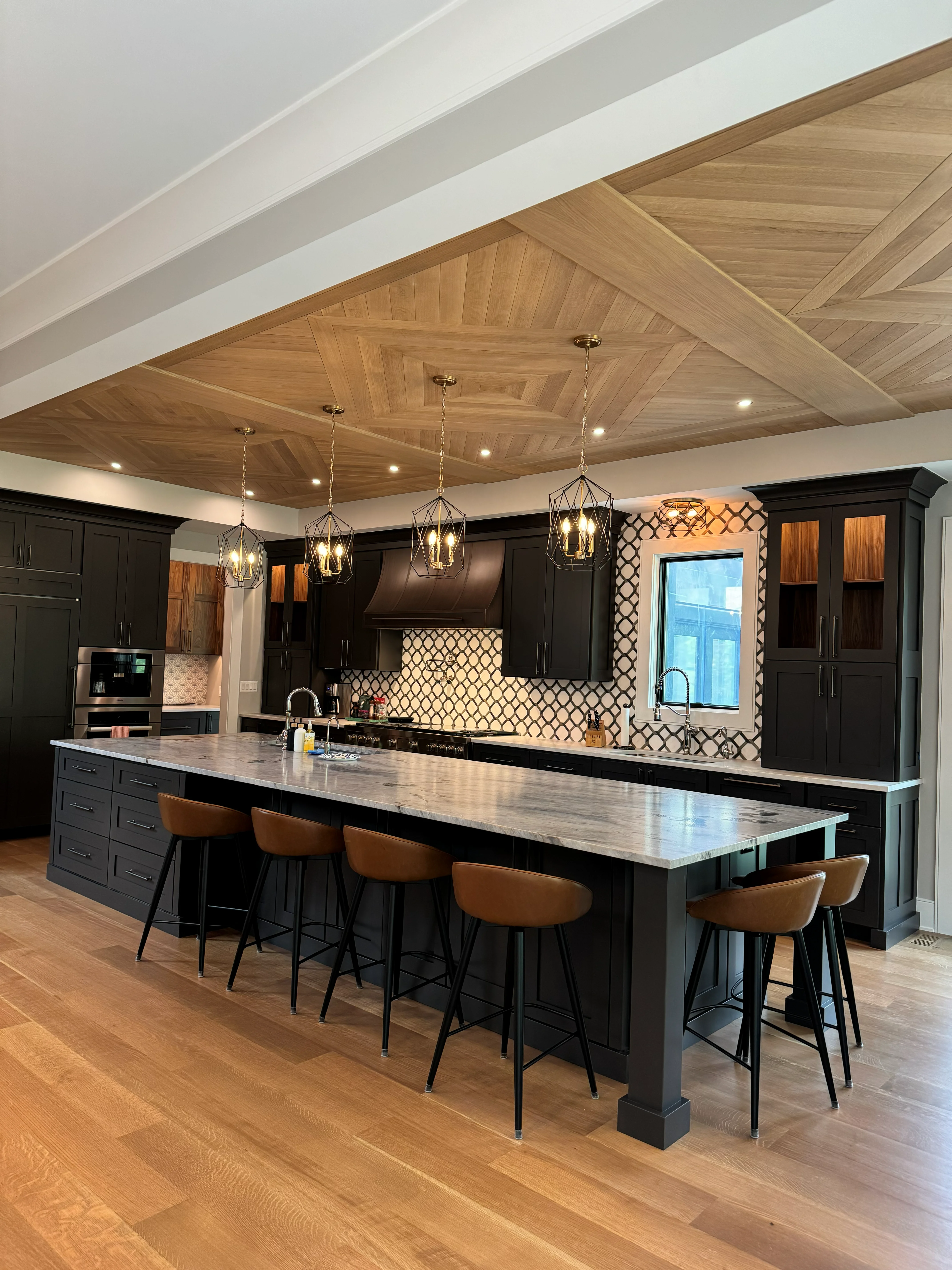 Black kitchen cabinets, herringbone wood ceiling, geometric tile backsplash, waterfall island with bar seating