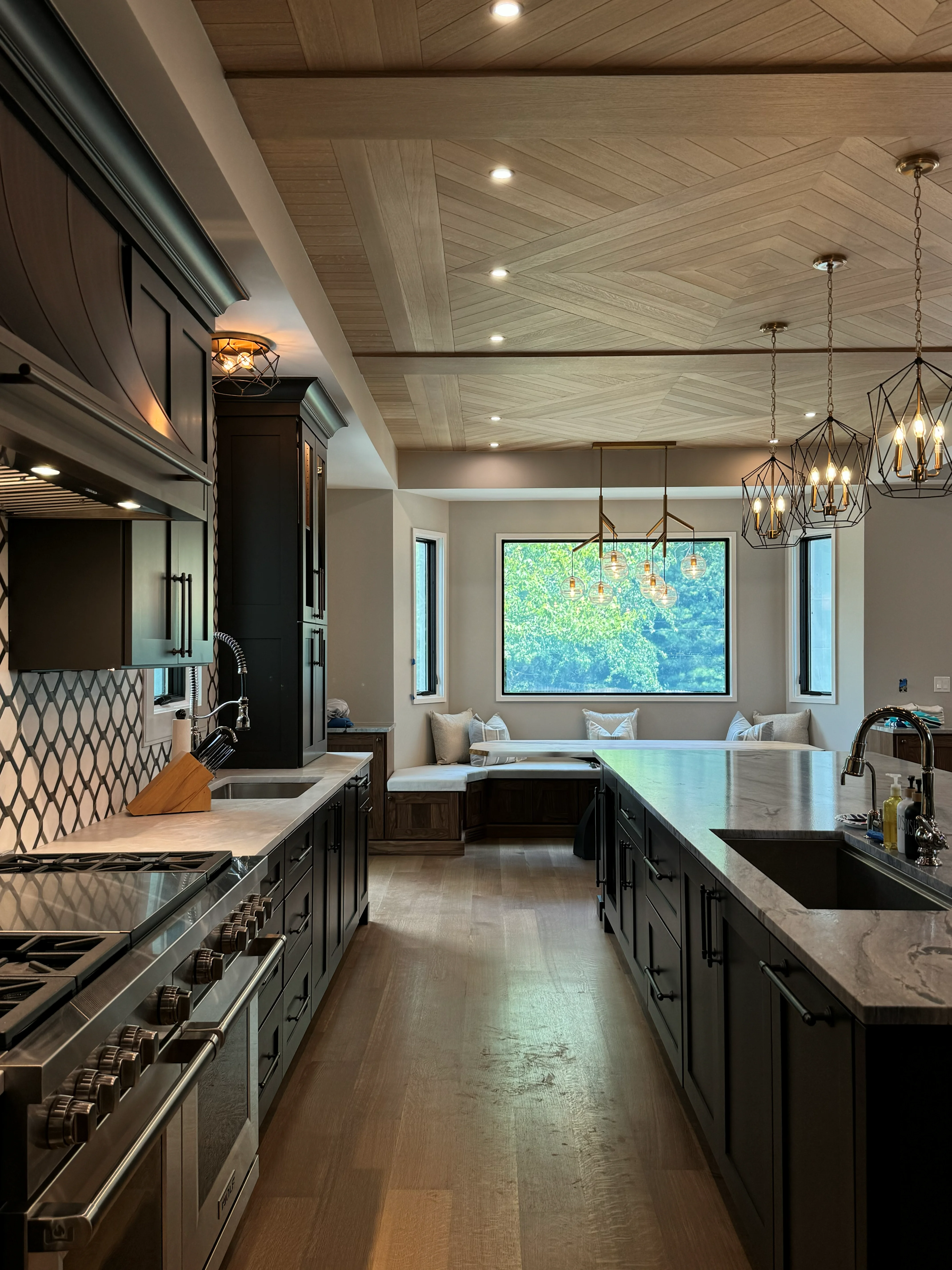 Modern kitchen with dark cabinets, marble counters, stainless steel appliances, herringbone ceiling, and pendant lighting