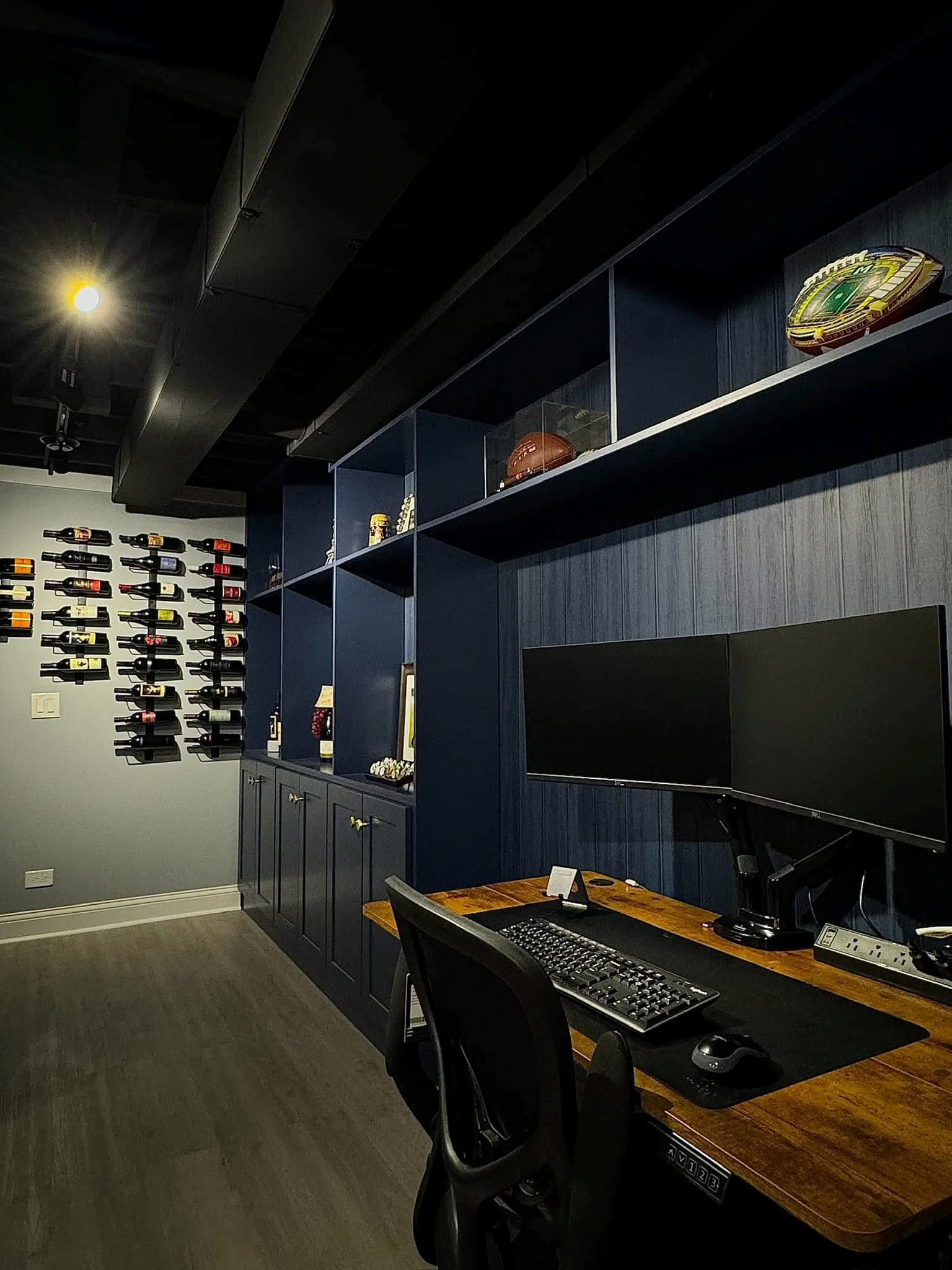 Finished basement with dark shiplap walls, floating shelves, wine storage, media wall, and wood desk