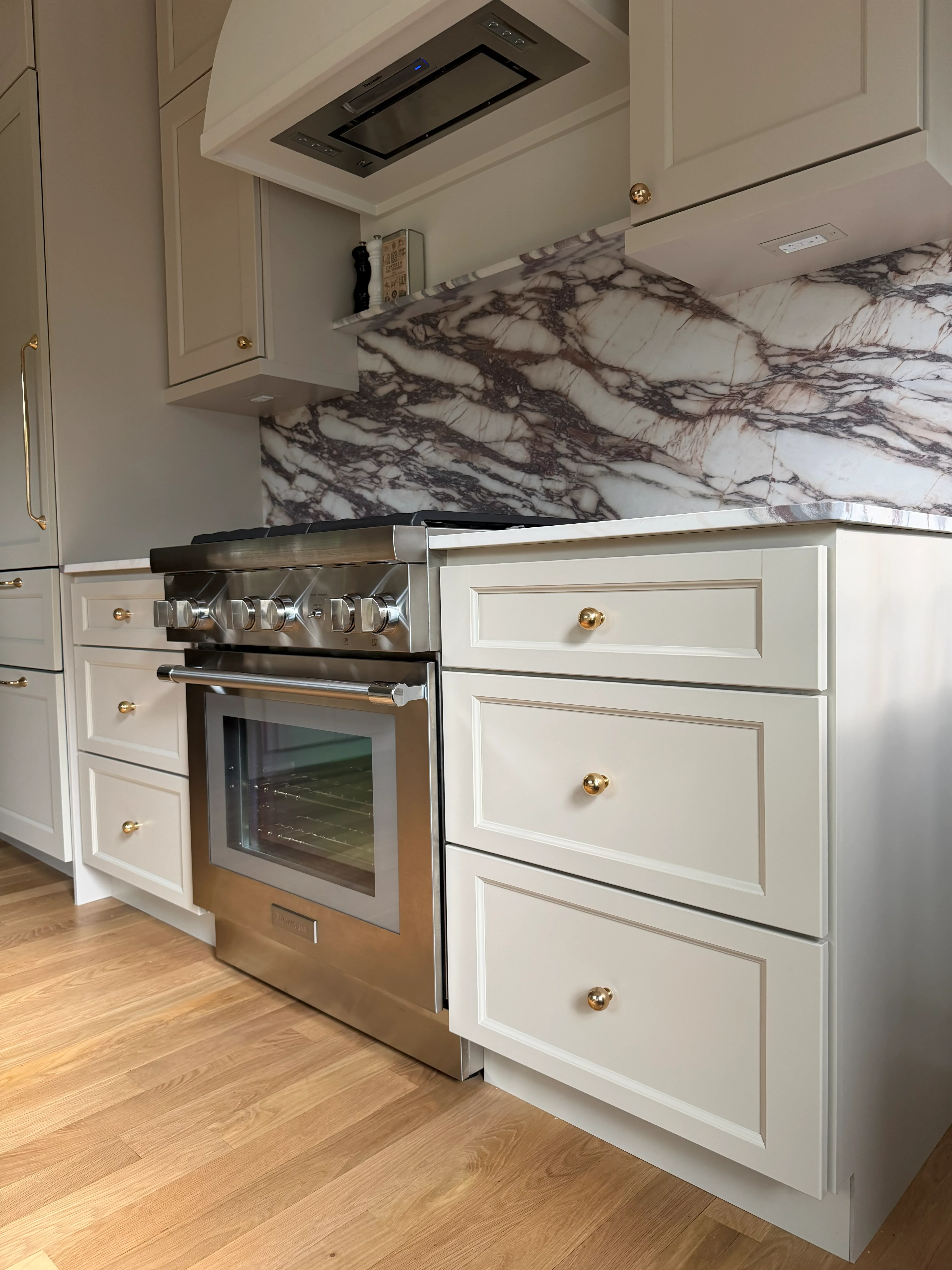 White kitchen cabinets with marble backsplash, stainless steel range, and hardwood flooring